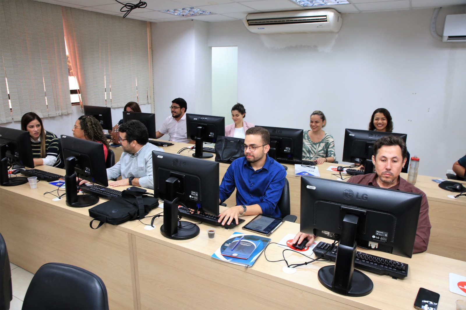 Na foto, vários alunos estão sentados na frente de seus respectivos computadores.